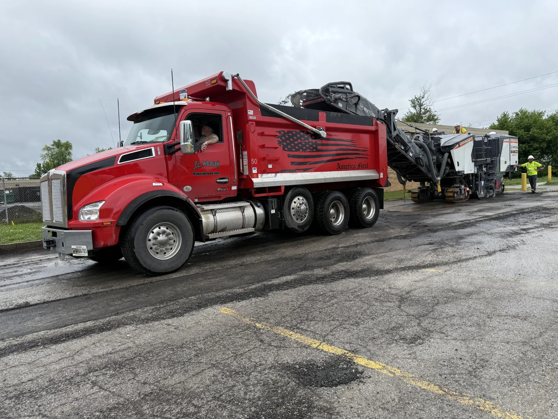 JL Wesley red tri-axle dump truck receiving asphalt millings from a road milling machine