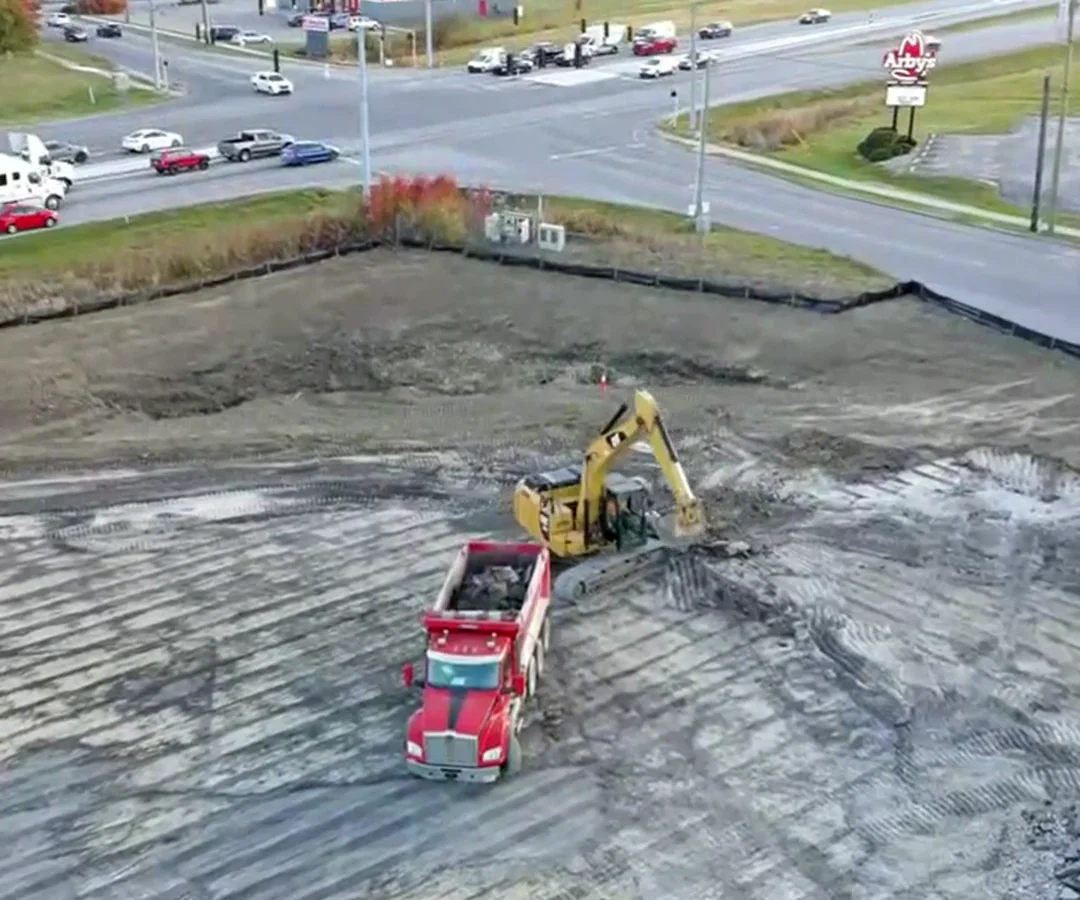 Aerial view of JL Wesley excavator loading a red dump truck on a commercial construction site
