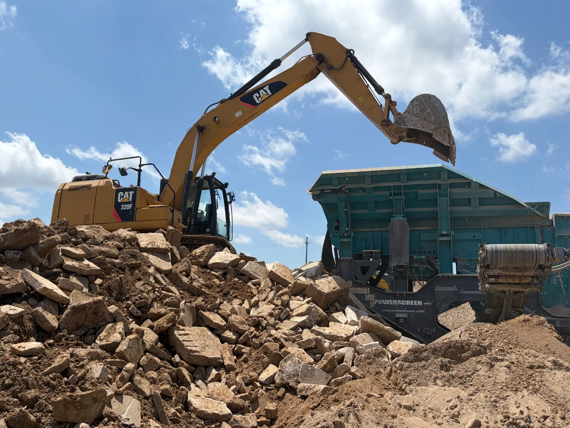 CAT excavator moving broken construction material into a green dump truck