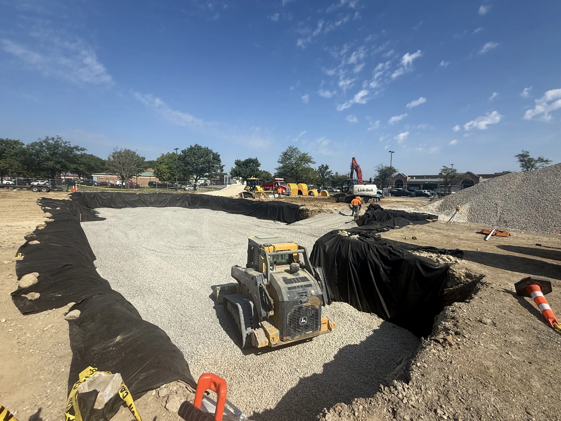 Compact track loader working on an aggregate base in an excavation lined with geotextile fabric